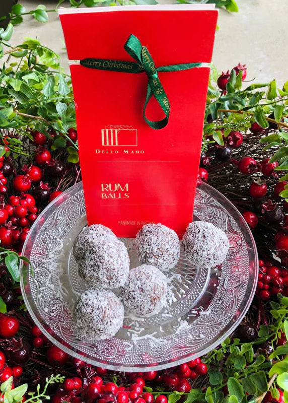 Red gift box with 'Rum Balls' on a glass plate surrounded by red berries and greenery