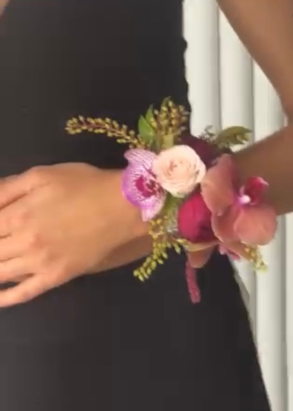 Close-up of a floral wrist corsage on a person wearing a black outfit.